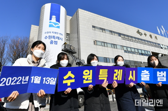 지난해 1월 특례시 출범을 앞두고 수원시청에 대형 현수막이 게시된 가운데 수원시 직원들이 특례시 출범을 축하하는 카드를 들고 있다.