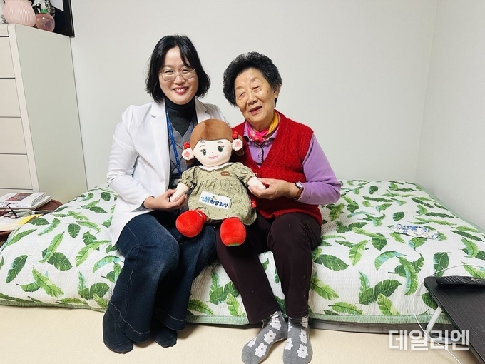  화성시동탄보건소 관계자와 독거 어르신이 AI 돌봄로봇 ‘효돌이’를 함께 들고 환하게 웃고 있다.